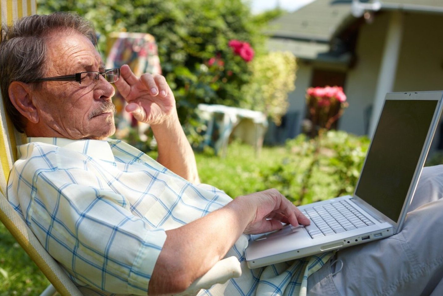 Un señor mayor usa su computadora portátil sentado en el jardín de su casa