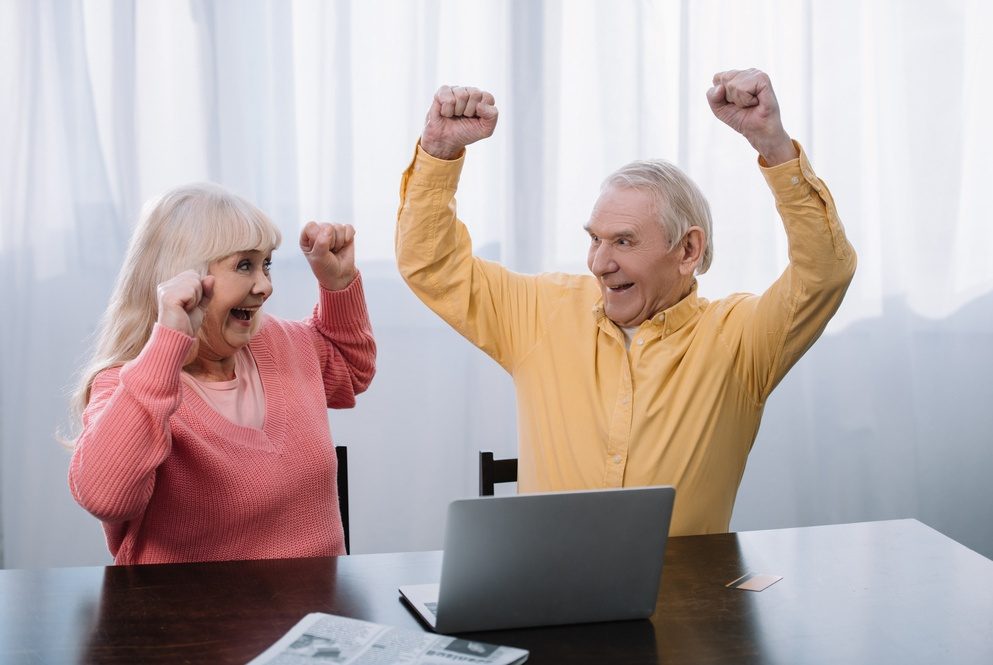 Una pareja de adultos mayores celebra frente a su computadora portátil