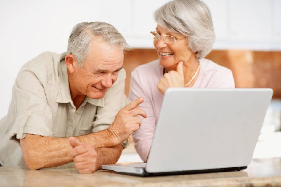 Una pareja de adultos mayores sonríe frente a una computadora portátil